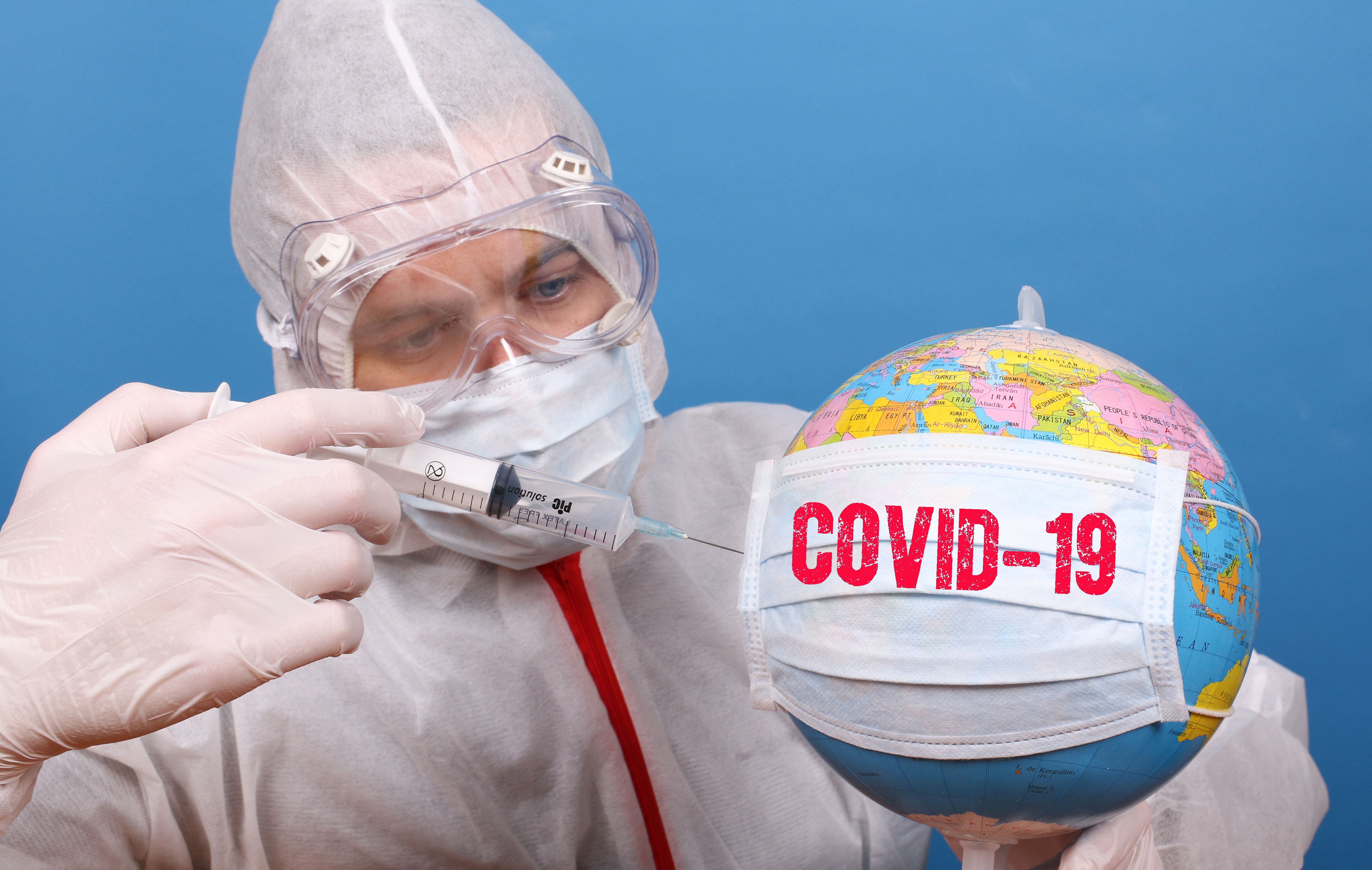 Photo showing a person waering a clinial protective suit injecting something with a syringe into a globe with the words COVID-19