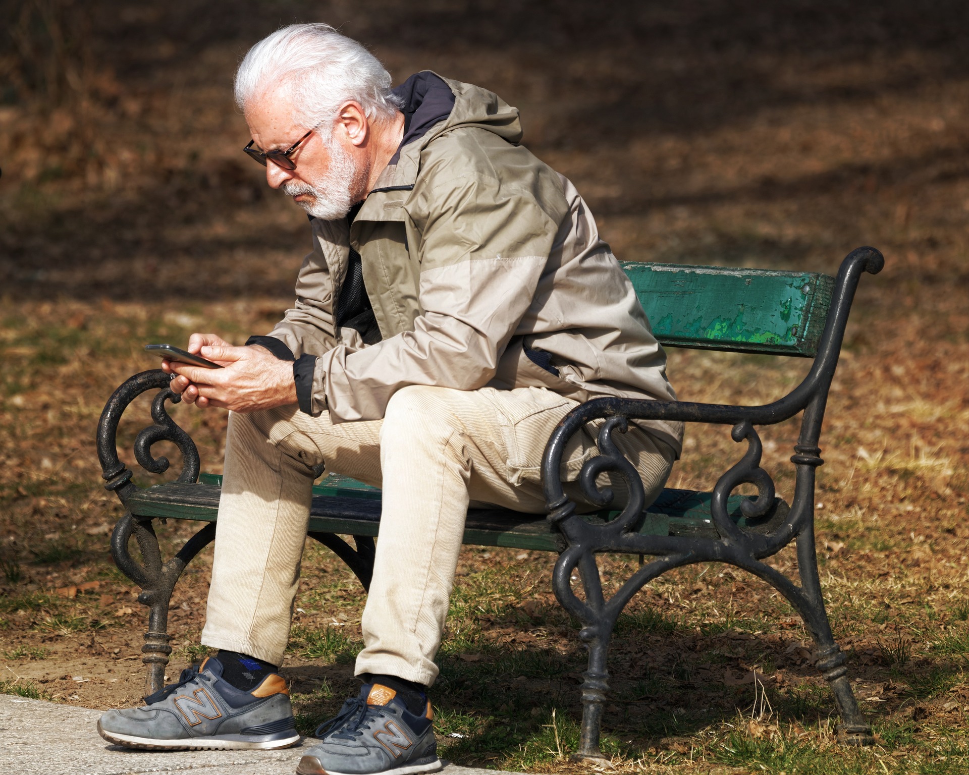 Photo of an older man sitting on a bench with a smartphone in his hand