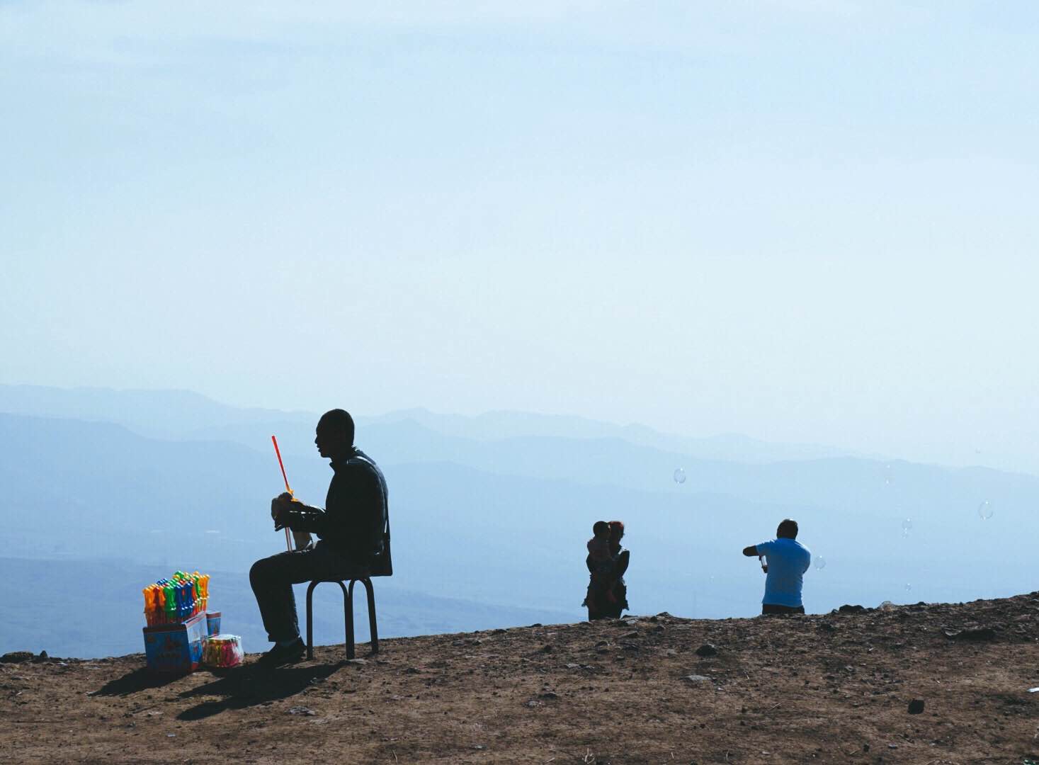 Man sitting atop a mountain with a vast view behind.